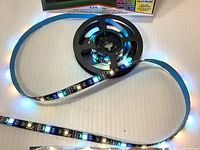 Rolled LED strip partially unrolled showing multi-color and white LEDs lit on a black strip base.