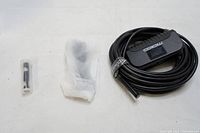 Photo showing the coiled flexible cable with camera head and small plastic accessory next to it on a white surface.