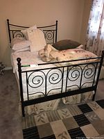 Black metal double bed frame with ornate spiral scrollwork headboard and footboard, partially made up with bedding and pillows to show size and style.