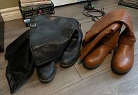 Two pairs of women's boots, black and brown, placed side by side on a wooden floor.