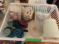 Wide shot of candles and ceramic tea light holders in white basket. Includes blue candles in glass holders, red votive, white scalloped candle, white jar candle, and white ceramic owl and lattice design tea light holders