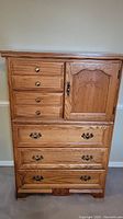 Front view of wood dresser showing five drawers on the left and one cabinet door with floral carving on the right.
