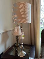 Photo of metal base table lamp with fabric shade featuring leaf patterns, placed on a glass-top side table.