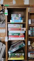 Shelf with stacked boxed puzzles in various sizes and colors. Titles and piece counts visible on some boxes, including Ticket to Ride: Europe and Winter Fence puzzles.