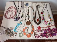 Photo of assorted costume jewelry necklaces laid out on a white surface showing various styles and colors, including beaded and pendant necklaces.
