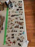 Full view of the collection of over 30 pairs of earrings laid out on a table, showing variety in styles and colors.