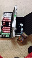 Two open metal cases showing multiple colored poker chips, several dice, and dealer buttons. Cribbage board box placed next to cases.