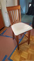 Front and side view of wooden bar stool with vertical slat back and white upholstered seat.