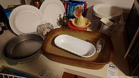Photo showing large stone baking dish, white milk glass bread dish, metal pie pans, yellow juicer, ceramic creamer, white plastic container, crystal clock, and some white plastic plates.