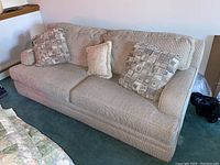 View of the beige Broyhill couch with three cushions on blue carpeted floor near a wooden ledge.