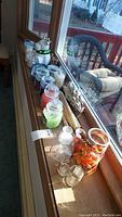 Wide-angle photo of candles and holders arranged on a window ledge showing three Yankee Candle jars in different colors, bundles of candle sticks, various glass candle holders and a decorative jar with autumn leaves and ribbon.