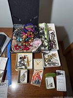 Overview of costume jewelry pieces displayed on a wooden surface, showing multiple necklaces, bracelets, earrings, and brooches in various boxes and loose piles.