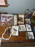 Photo of all costume jewelry items arranged on a wooden surface showing necklaces, boxes with bracelets, earrings, and a jewelry container.