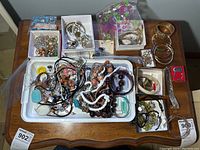 Wide shot of all costume jewelry on wooden table showing mix of bangles, bracelets, earrings, and necklaces in trays and loose