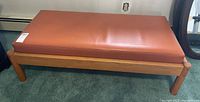 Front angled view of mid century modern style ottoman with wooden frame and brown leather cushion showing overall condition.