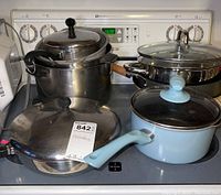 Photo showing stainless steel pots and pans with one light blue pot and pan with lids, arranged on stove top.