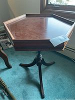 Angled view of the hexagonal wooden side table with visible surface scratches and carved pedestal base with claw feet.
