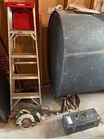 Wide shot showing the aluminum ladder, metal toolbox, corded circular saw, power drill and additional hand tools on the floor and in a container