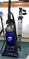 Full view of upright Hoover WindTunnel vacuum cleaner and Bogen Manfrotto tripod placed side by side.