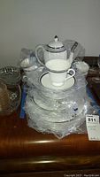 Stack of plates, cups, saucers wrapped in original plastic sleeves with coffee pot behind