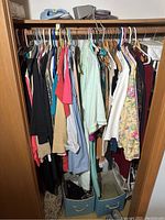 Wide view of closet showing vintage women’s clothing in various colors and fabrics hanging on a rod with storage baskets below