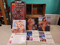 Photo of the lot showing the sealed 2005 Jeff Gordon NASCAR wall calendar in original plastic packaging with frame, and open vintage pin-up calendars by Ridgid and Anna Nicole Smith 1996 calendar includes March 1996 page.