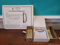 Appraisal certificate and bangle in presentation box showing full lot contents and appraised documentation.