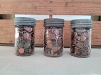 Front view of three Crown Mason jars filled with pennies, showing the metal lids and clear glass bodies packed with coins.