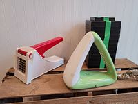 Photo showing plastic potato chipper with red lever and retro green and white triangular-shaped telephone side by side on wooden surface.