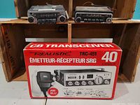 Front view showing the Realistic TRC-451 CB Transceiver box with image and text, and two vintage car radios placed on a wooden crate shelf above it.