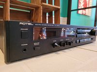 Close-up angle of front left side of the receiver showing power button, headphone jack, bass, treble, and balance control knobs, branding and model.