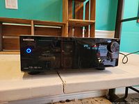 Front view of the Samsung AV-R720 receiver powered on with blue power indicator light and digital display.