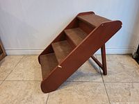 Wooden folding pet steps with a reddish-brown finish, carpet-covered steps, shown from side angle on tiled floor.