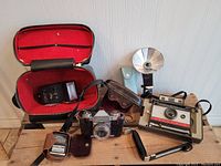 Wide view showing Polaroid Land Camera 220, Weston light meter, two flashes, Zeiss Ikon Contaflex camera with case, and red-lined carrying case.