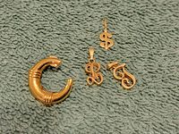 Photo of four 14k gold jewelry pieces: bangle bracelet and three pendants on green textured fabric background.