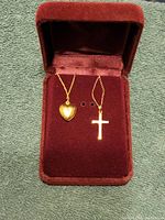 Two 14k gold necklaces in a jewelry box, one with a heart-shaped locket and one with a cross pendant, shown with coin for size reference.