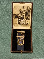 Shows full medal including blue ribbon inside vintage box with photo attached to box lid.