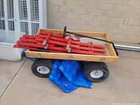 Wooden wagon with red slatted sides, large black air-filled tires, and black metal pull handle shown from above side angle.