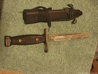 Full view of bayonet and sheath laid side by side on fabric surface.