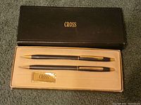 Box with Cross logo on top, containing two black and gold writing instruments and a Cross label inside.