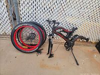 Electric bike frame and two Kenda brand tires leaning against chain link fence