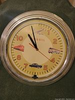 Front view of Fossil wall clock showing dial with vintage vehicle illustrations and silver frame.
