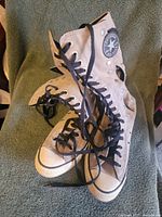 Pair of beige high top Converse sneakers shown resting on a green towel, displaying overall appearance and condition.