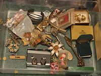 Full view of the assorted vintage jewelry and decorative spoons lot in a plastic container
