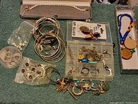 Overview photo showing pearl necklace boxed on top, various bangles stacked in center, loose pearl earrings in plastic bags, plastic container with assorted small jewelry, beaded necklace with wooden pendant on right.