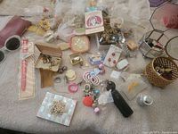 Overview of a table covered with assorted jewelry, vanity items, watches, and crafting materials scattered and partly wrapped in plastic bags.