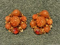 Front view of a pair of signed Judy Lee earrings showing coral-colored spherical beads and red faceted stones on a gold-tone setting.