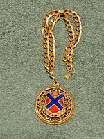 Gold tone double-link chain necklace laid out showing the round crest pendant with blue and red colors and Latin motto.