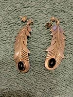 Front view of the pair of sterling silver feather earrings with black onyx stones at the base of feathers.
