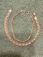 Two sterling silver bracelets on green towel, one thicker woven chain and one thin box chain.